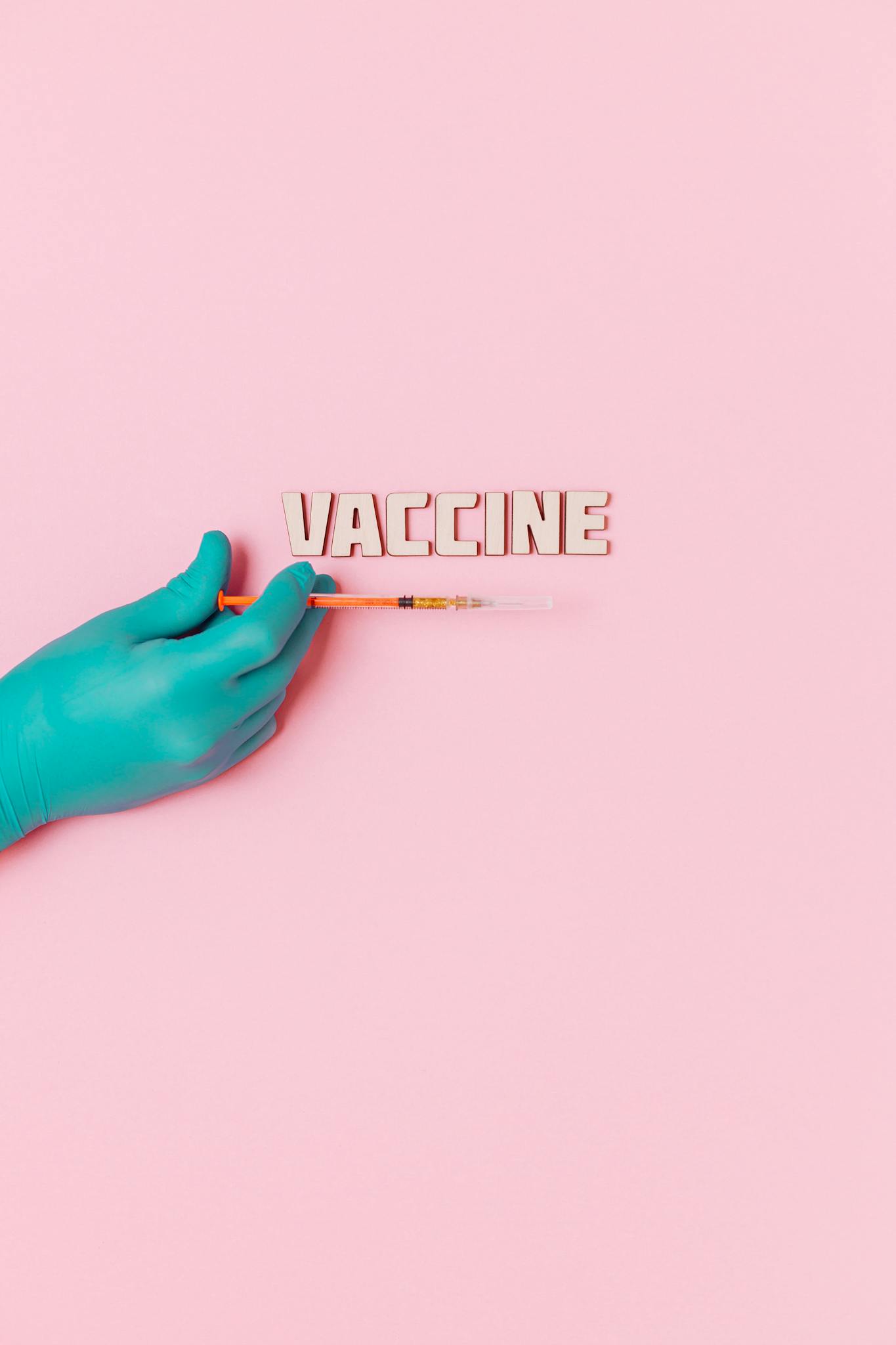 Vaccine Text and A Person Wearing Latex Glove While Holding a Syringe on Pink Background